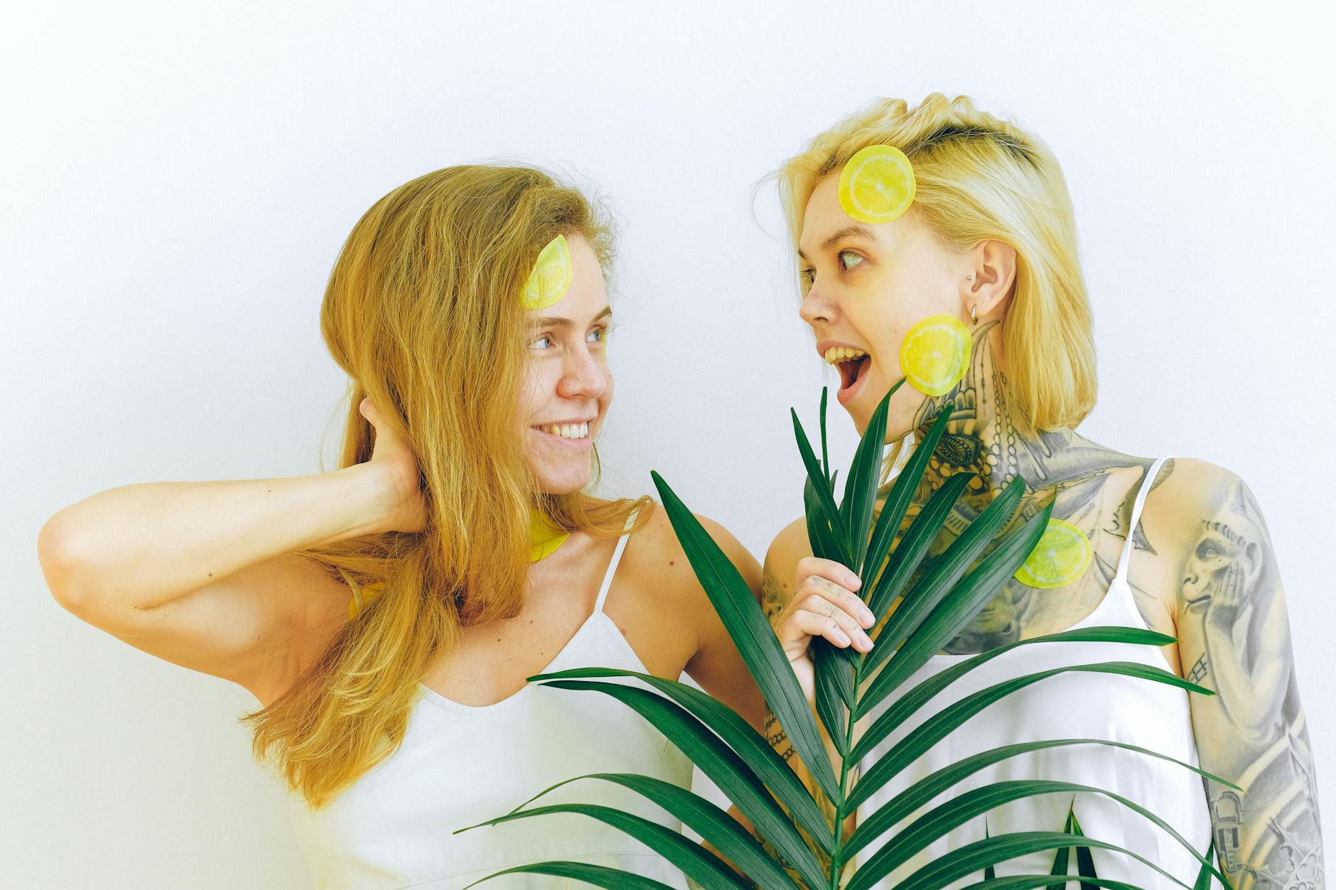 Deux femmes souriantes partageant un moment joyeux avec des tranches de citron et une plante tropicale, exprimant la connexion et le plaisir partagé