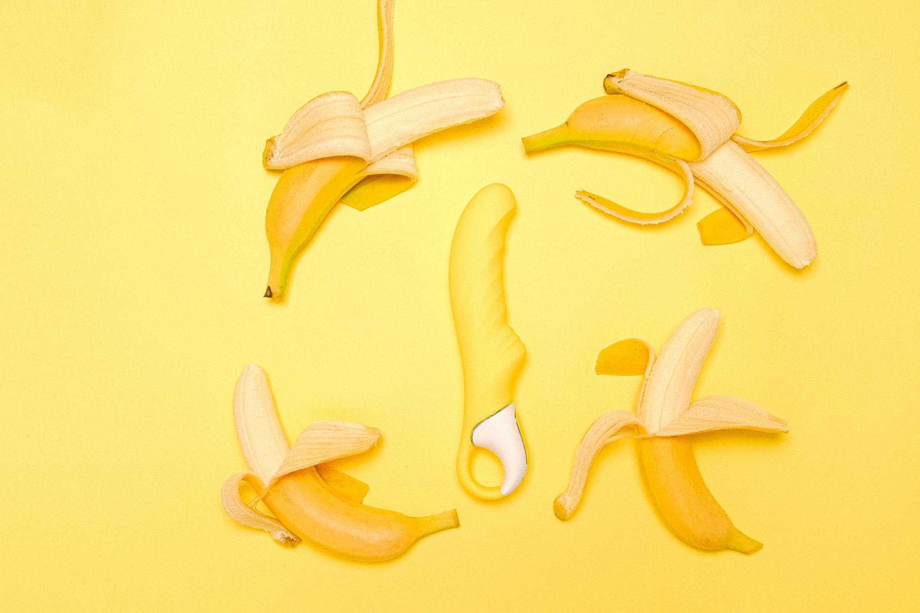 Photographie plate créative d'un vibromasseur jaune entouré de bananes pelées sur fond jaune