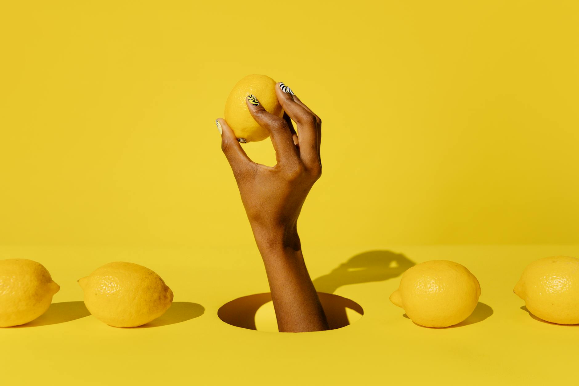 A hand holding a fresh lemon against a vibrant yellow background, symbolizing the bright, citrusy sensation of lemon vibrators after midlife