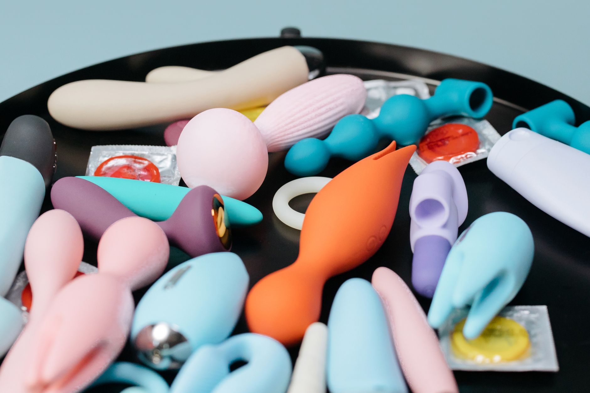 A person holding a basket containing colorful vibrators and a pink flower, symbolizing shared pleasure in relationships.