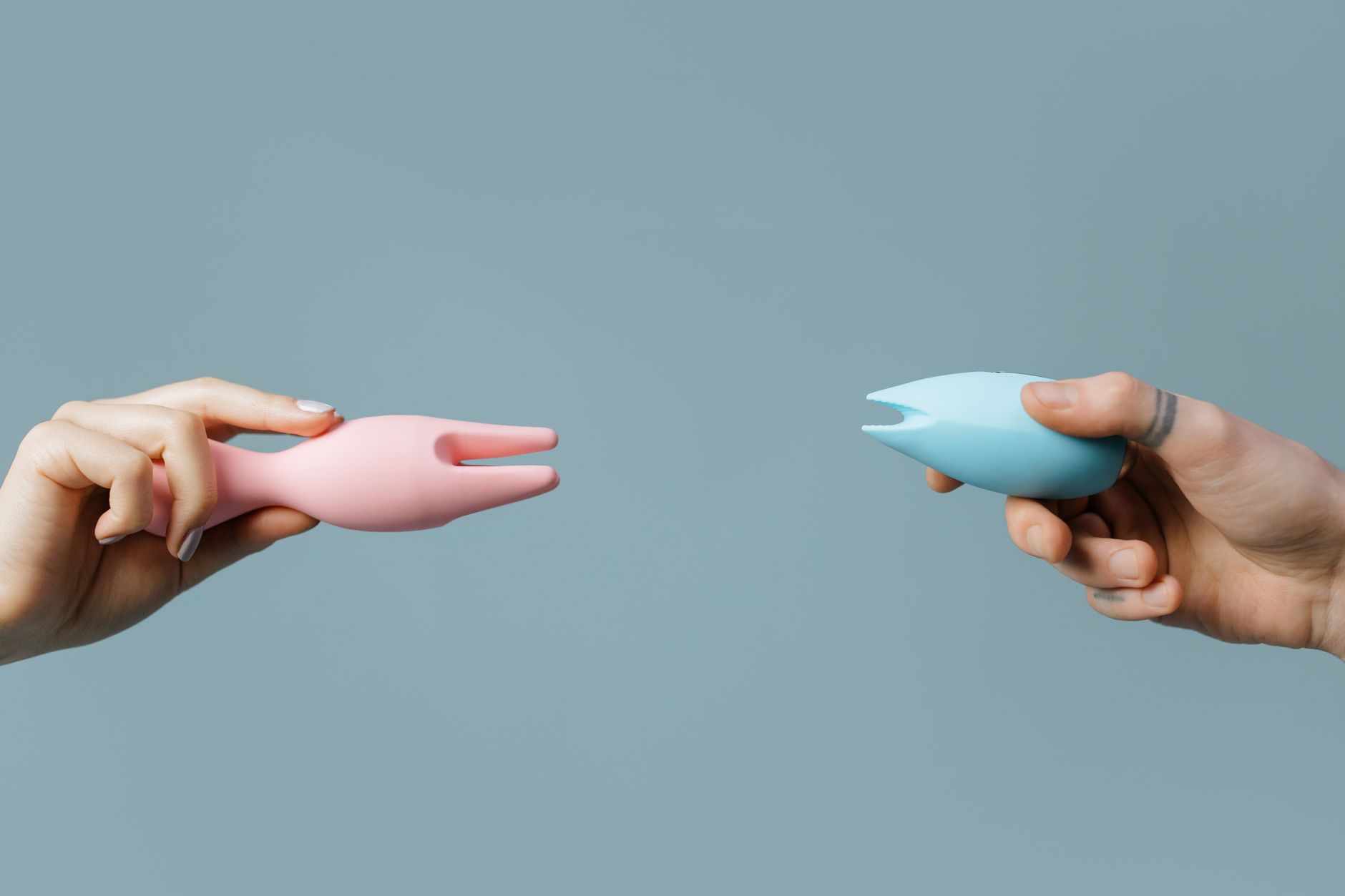 Two hands holding silicone vibrators against a soft pastel background