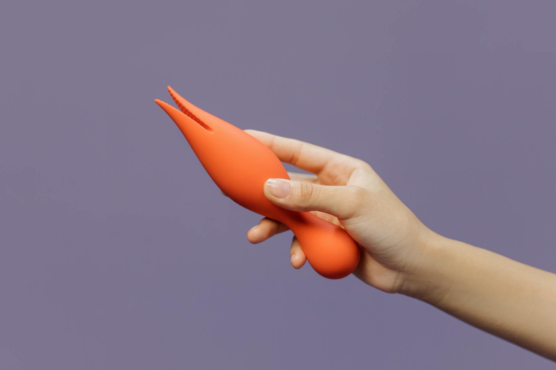 A hand holding a lemon clitoral vibrator against a minimalistic purple backdrop