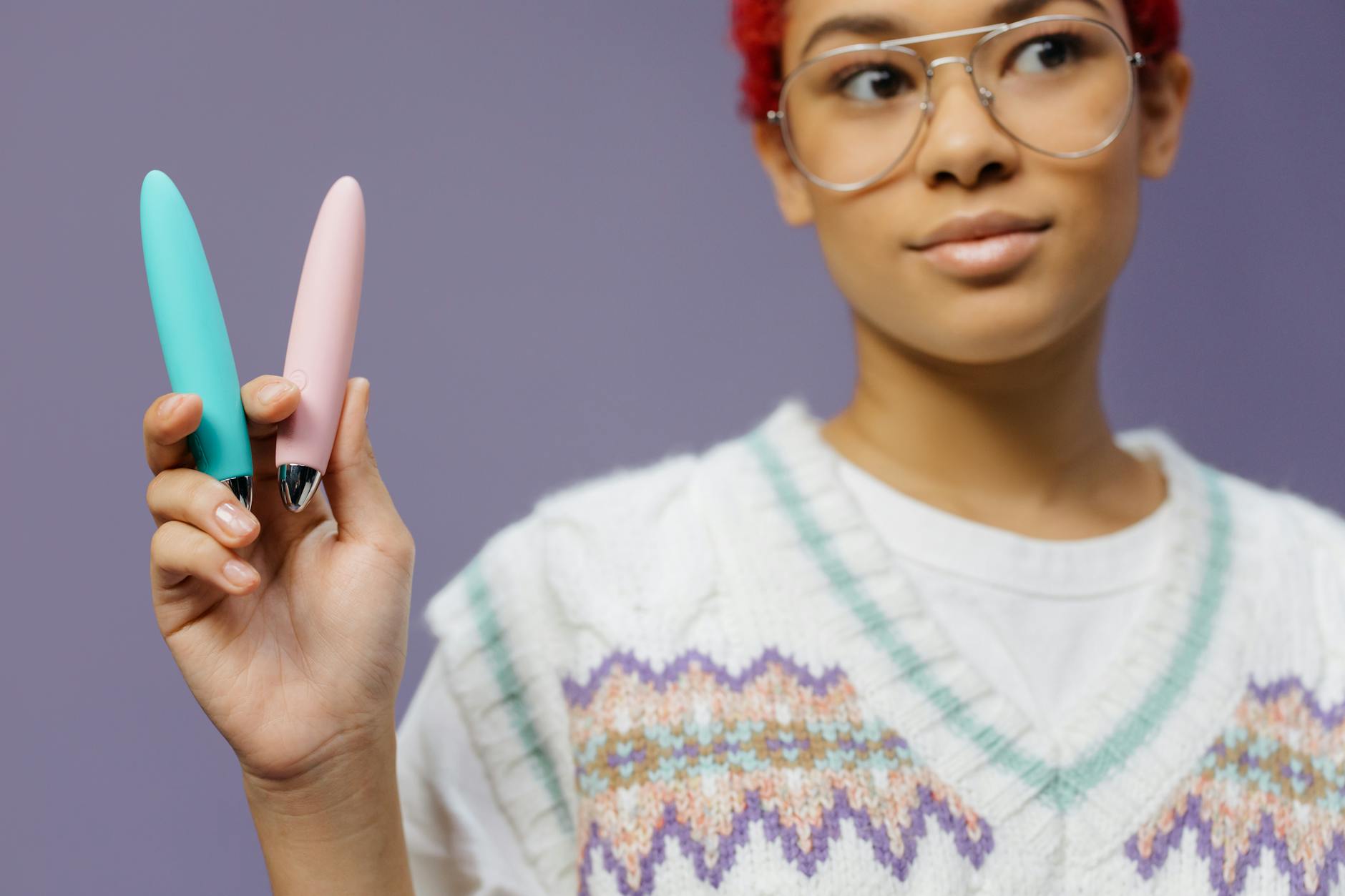 Two colorful vibrators held against a purple background, representing modern clitoral pleasure tools