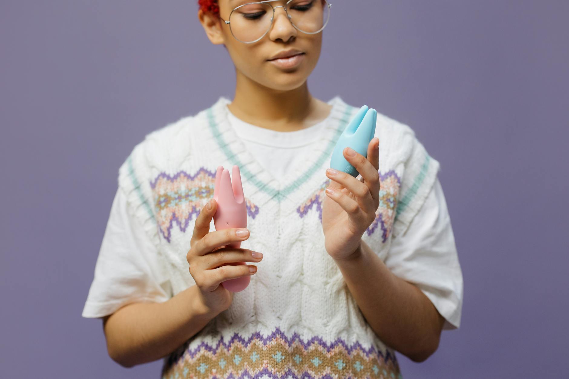 Woman holding blue and pink clitoral vibrators in contemplative moment