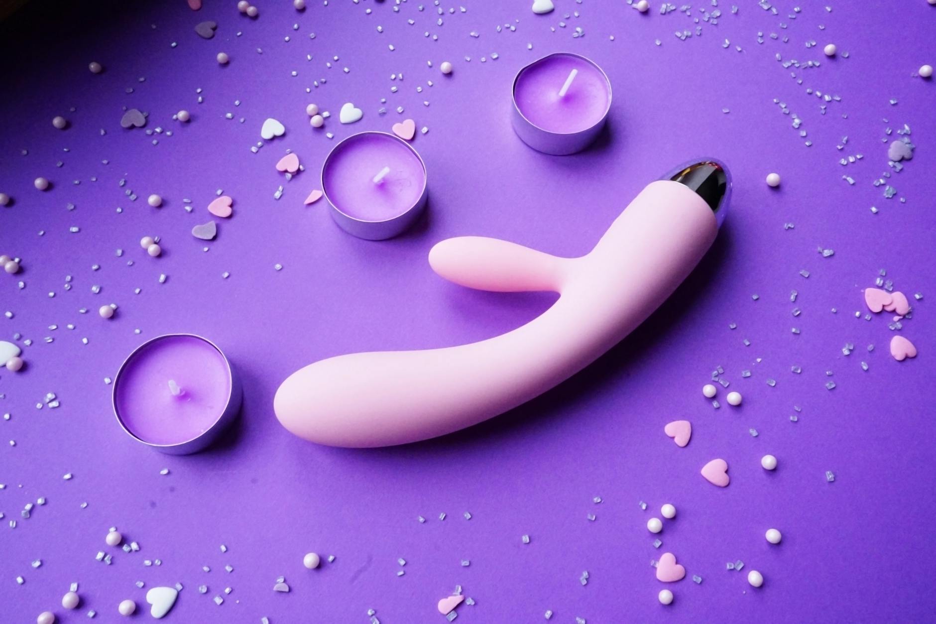 Pink vibrator surrounded by hearts and candles on a romantic surface