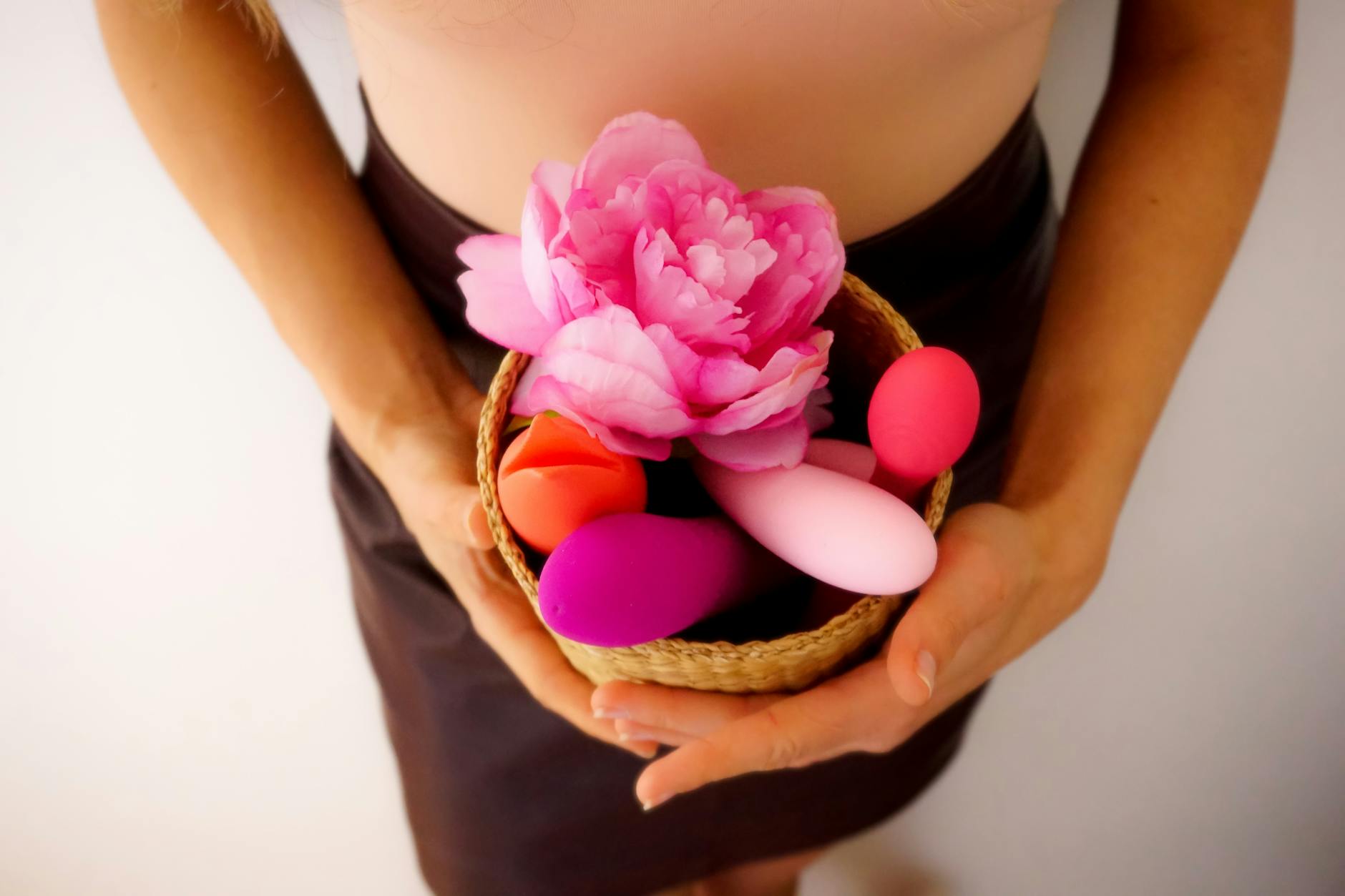 Two hands holding pink and blue silicone clitoral vibrators against a pastel background.